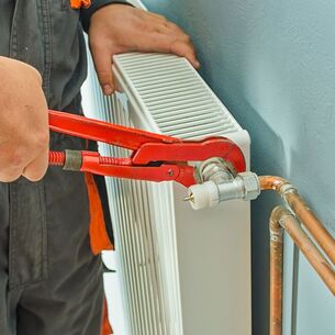 Heating technician using red wrench to adjust pipe setting for radiator heater attached to wall